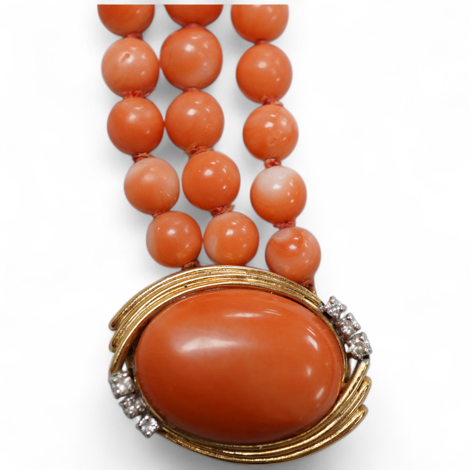 A coral necklace, composed of three strands of coral beads measuring approximately 5.1-6.6mm diameter, to a gold clasp set with a coral cabochon and brilliant-cut diamonds, mounted in gold, length 45.5cm, stamped 14K, ca